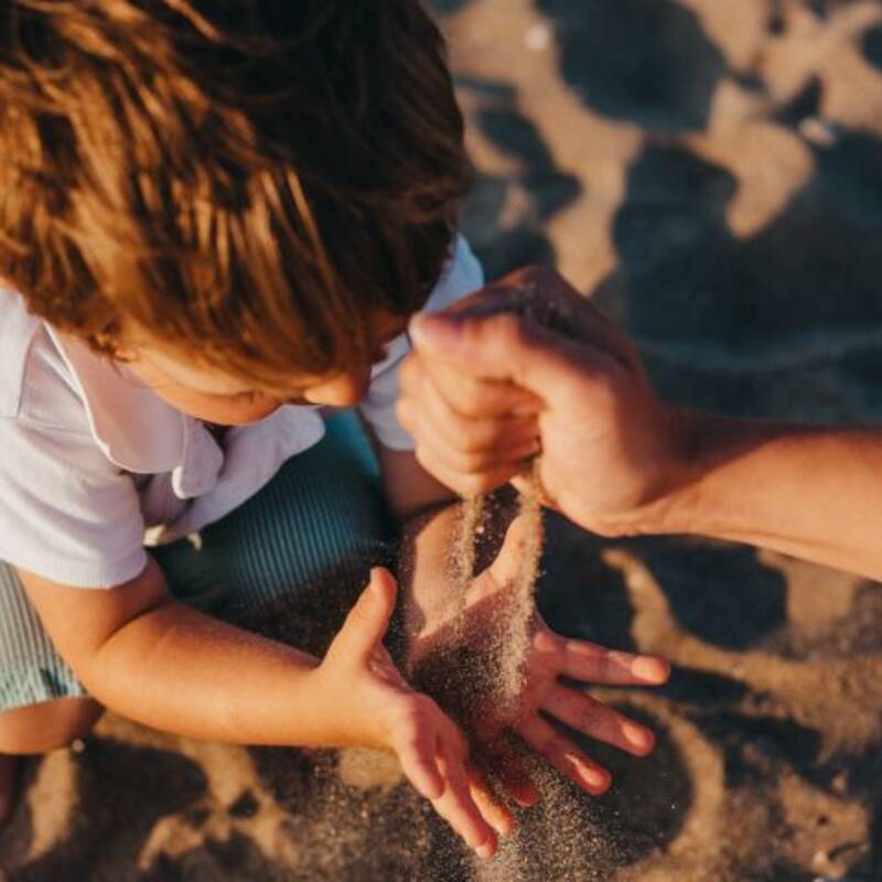 Sand rinnt durch eine Hand in die Hände eines Kindes