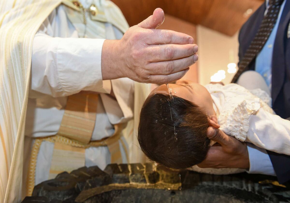Priester benetzt die Stirn des Kindes mit Taufwasser