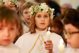 Mädchen mit Blumenschmuck bei Erstkommunion hält Kerze