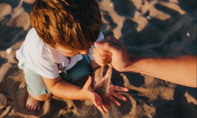 Sand rinnt durch eine Hand in die Hände eines Kindes